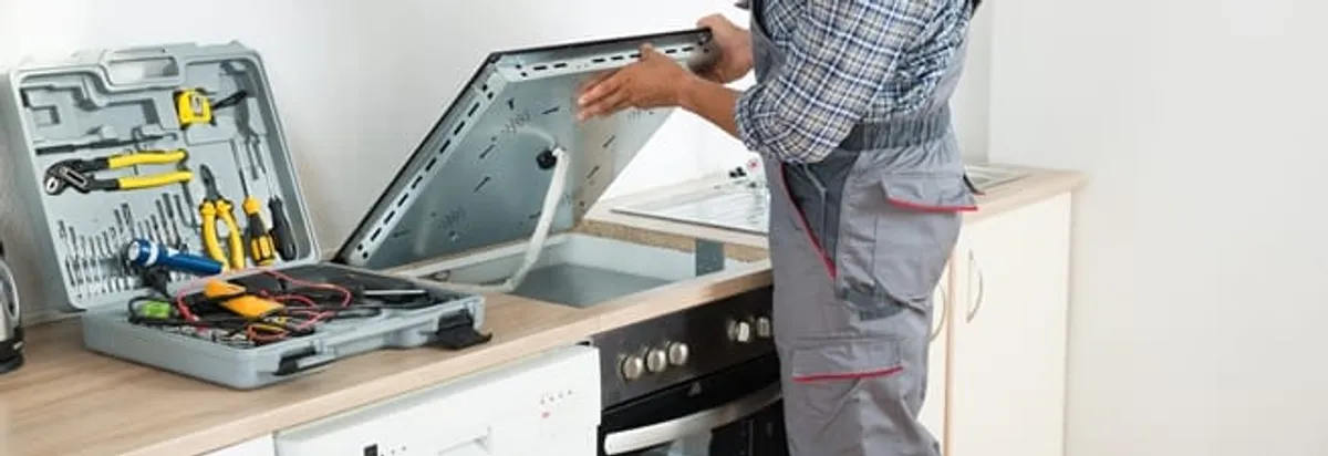 Cooktop repair technician lifting a built-in stovetop for service in Chattanooga, TN