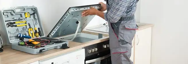 Cooktop repair technician lifting a built-in stovetop for service in Chattanooga, TN