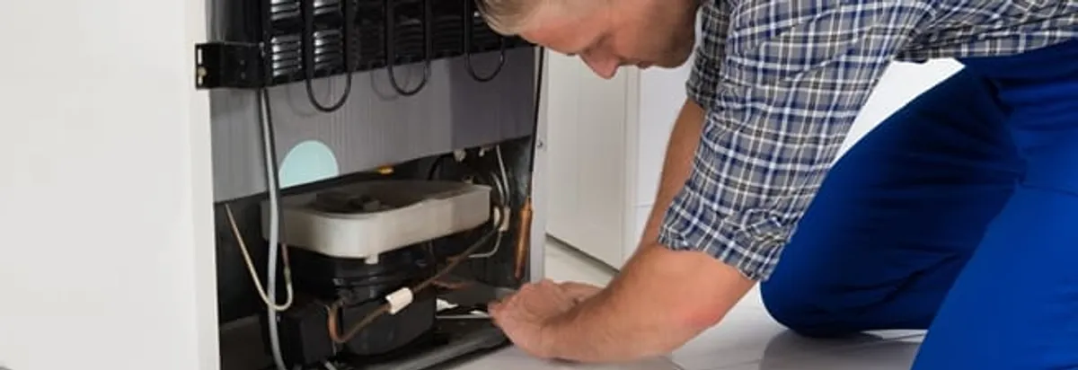 Refrigerator repair technician servicing the compressor and condenser area in Chattanooga, TN
