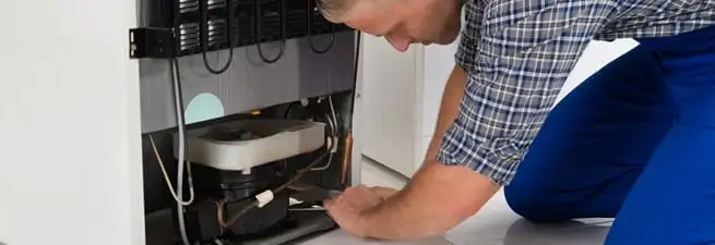 Refrigerator repair technician servicing the compressor and condenser area in Chattanooga, TN