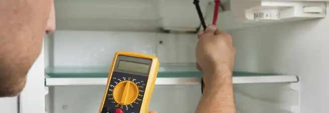 Refrigerator repair technician testing electrical components with a multimeter in Chattanooga, TN