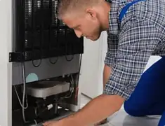 Refrigerator repair technician servicing the compressor and condenser area in Chattanooga, TN